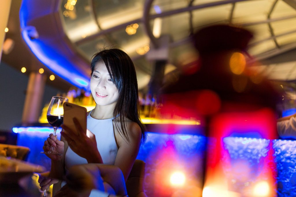 Woman use of mobile phone and enjoy her wine at sky bar. Source: Adobe Stock/Leung Chopan